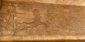 Battle of Kadesh relief showing Ramses II riding a chariot and fighting enemy forces in ancient Egypt.
