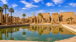 Karnak Temple – Luxor, Egypt: Gateway To Ancient Wonders 11 Sacred Lake at Karnak Temple in Luxor, Egypt, reflecting ancient sandstone temples, columns, obelisks, and palm trees beneath a blue sky.