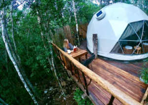White geodesic glamping dome with a wooden deck surrounded by dense tropical rainforest.