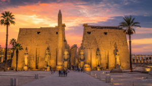 Karnak Temple – Luxor, Egypt: Gateway To Ancient Wonders 17 Luxor Temple in Egypt illuminated at sunset, featuring an ancient obelisk, monumental pylons, pharaoh statues, sandstone columns, and palm trees.