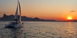 ✨ Rio De Janeiro Glamping Hub: Luxury Nature Stays in Brazil’s Most Vibrant City 12 Sailboat cruising across the waters near Rio de Janeiro at sunset, with golden reflections on the ocean and mountains silhouetted against the evening sky.