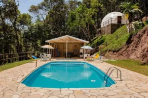 Atlantic Forest Safari Tents in Juquitiba: Luxury Glamping Amidst Nature 2 Outdoor swimming pool surrounded by lush forest with a hillside glamping dome and relaxing lounge area in Juquitiba, Brazil.