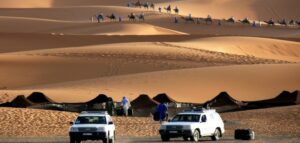 Two jeeps at a sandy desert with people on camels for desert safari.