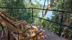 🌿 Selva Boutique Tents: Stylish Glamping Amidst The Iguazu Rainforest 3 Two chairs on a balcony overlooking a lush rainforest with a river flowing through the landscape.”