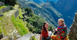 🏞️ Luxury Royal Inca Trail (4 Days) – Exclusive Trekking Experience 4 Two girls sitting on a mountain at an ancient ruin location with trees and vegetation and steep mountains.
