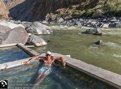 Person in a pool next to a creek with large boulders and a mountain.