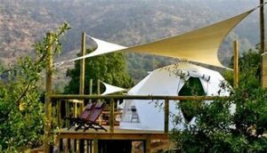 Glamping dome on a platform on a porch with chairs and trees and mountains.