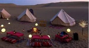 Duna Camp – Huacachina, PeruHidden Among the Golden Dunes 1 Two glamping tents in a desert with places to sit on pillows in a desert with lights lighting up the camp.