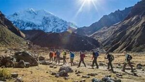Several people on a trail with backpacks in a valley with mountains on a sunny day.