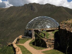 Glamping dome on a hill with large windows and a towering mountain in the background.