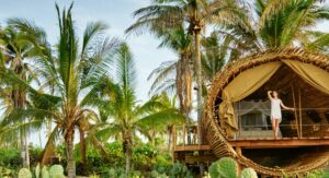 Woman standing on the wooden deck of a glamping structure in a lush rainforest, with an outdoor bed behind her.