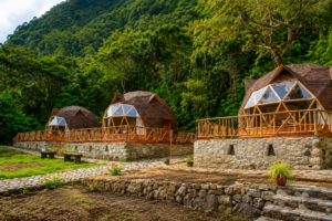 Luxury glamping dome cabins surrounded by lush green mountain rainforest near Machu Picchu, Peru. The image features beautifully designed wooden-and-glass geodesic domes with spacious decks, stone pathways, colorful landscaping, and scenic forest-covered mountain slopes creating a peaceful eco-lodge retreat in the Andes.
