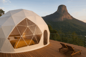 Glamping dome in a rainforest on a platform with a chair and a mountain.