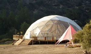 Large geodesic glamping dome with transparent panels and a wooden deck surrounded by rugged mountain vegetation in Cajón del Maipo, Chile.