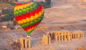 Hot air balloon with people flying over ancient ruin location in a desert in Egypt