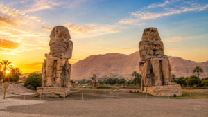 Karnak Temple – Luxor, Egypt: Gateway To Ancient Wonders 20 Colossi of Memnon near Luxor, Egypt, featuring two enormous ancient stone statues with desert mountains and palm trees at sunset.