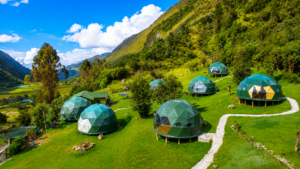 Colorful mountain valley glamping resort near Cusco, Peru, featuring multiple geodesic dome accommodations surrounded by lush green hills, scenic walking paths, forests, and breathtaking Andes Mountain views.