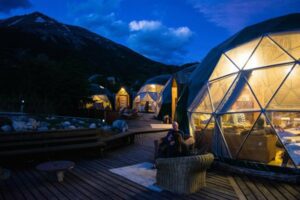 Person sitting in a chair with several glamping domes with large windows on a wooden deck at night.