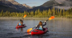 Two people canoeing on a lake with a forest and mountains in the background
