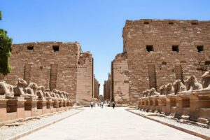People at Karnak Temple with two rows of statues and a walkway at an ancient ruin location.