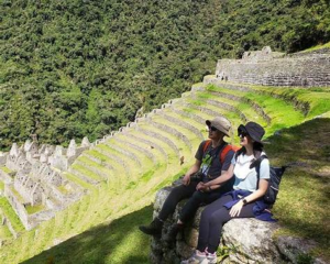 Travelers relaxing beside ancient Incan terraces near Machu Picchu surrounded by lush green mountain scenery along the Royal Inca Trail in Peru.