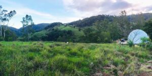 Nature Domes In Lunahuaná Valley 1 Glamping dome in a field near a woods with vegetation and a mountain.
