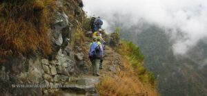 🏞️ Luxury Inca Trail Tours (4 Days) – Trek In Style 3 Several people with backpacks walking on a trail up a hill with trees and vegetation.