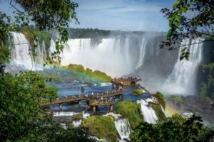 Iguazu Fall in a rainforest with tourists on a long bridge.