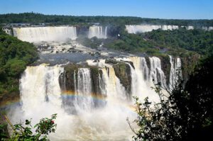 Aerial view of Iguazú Falls cascading through dense green rainforest, with mist rising above the river.