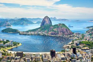 Aerial view of Rio de Janeiro, Brazil, showing the dense cityscape with numerous buildings and the ocean in the background.