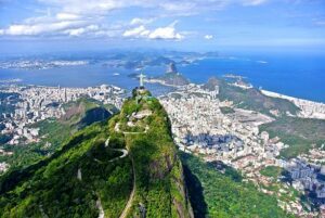 Aerial view of Rio de Janeiro, Brazil, showing city buildings, the Christ the Redeemer statue, and the ocean.