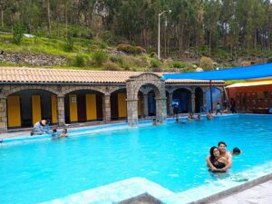 People in as pool at a hotel with a hill and trees in the back ground.