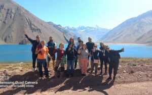 Group of people standing with a lake behind them and steep tall mountains.