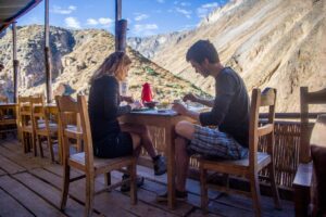 people easting at a table with food and chairs under a canopy with mountain view.