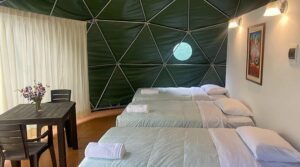 Inside a glamping dome with three beds with a table and chairs and curtains