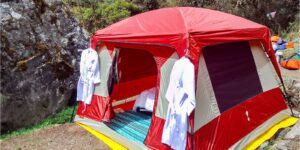 Glamping Tent with clothes on hangers and a bed inside with trees and large boulders.