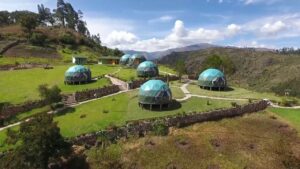 Glamping domes on a hill with tees and vegetation with stone walls and mountains
