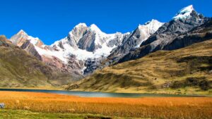 Flat field with a river and steep hills and tall mountains with white snow covered.