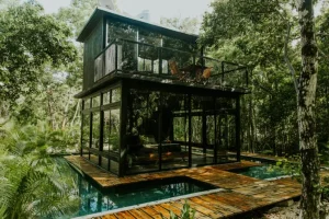 ✨ Rio De Janeiro Glamping Hub: Luxury Nature Stays in Brazil’s Most Vibrant City 16 Modern two-story glass treehouse surrounded by lush tropical rainforest, featuring a wooden deck, outdoor seating, and reflecting pools.