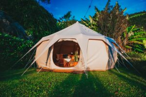 Luxury canvas glamping tent with a comfortable bed and warm interior surrounded by lush tropical vegetation.