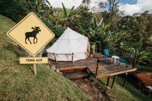 Canvas glamping tent on a raised wooden deck surrounded by lush tropical vegetation and mountain scenery in Brazil.