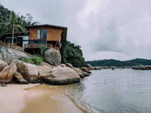 Cliffside accommodation overlooking a quiet rocky beach and coastal waters surrounded by tropical vegetation in Florianópolis, Brazil.