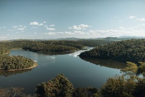 Guararema Riverside Glamping, Brazil: A Peaceful Escape by the Water 4 Peaceful winding waterway surrounded by lush green forests, rolling hills, and distant mountains beneath a blue sky, illustrating the natural beauty of riverside Brazil.