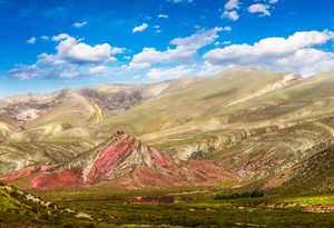 Glamping In Cajón Del Maipo: Andes Luxury Camping Near Santiago, Chile 1 Colorful Andes mountain landscape featuring red and pink rocky hills, rolling golden-green slopes, a lush valley, and a brilliant blue sky with scattered white clouds.