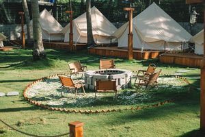 Boutique Safari Tent, Leme – Stylish Beachside Glamping Near Copacabana 3 Luxury canvas glamping tents on wooden platforms surrounding an outdoor fire pit with camping chairs, green lawns, and tropical trees.