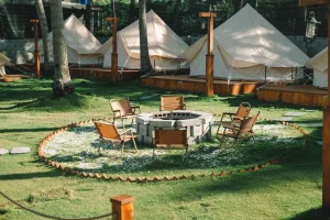 ✨ Rio De Janeiro Glamping Hub: Luxury Nature Stays in Brazil’s Most Vibrant City 22 White safari-style glamping tents on raised wooden platforms surrounding a grassy courtyard with outdoor chairs and a circular stone fire pit.