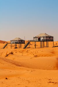 Luxury Tents in Huacachina Oasis: Desert Glamping & Adventures in Peru 4 Two elevated luxury safari-style tents on raised platforms with stairways, surrounded by sweeping golden-orange sand dunes in a desert landscape
