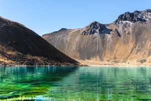 Glamping In Cajón Del Maipo: Andes Luxury Camping Near Santiago, Chile 3 Crystal-clear turquoise mountain lake surrounded by rugged Andean peaks, rocky slopes, and snow-dusted summits beneath a bright blue sky.