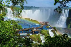 Visitors standing on a platform overlooking Iguazú Falls surrounded by lush rainforest and cascading waterfalls.