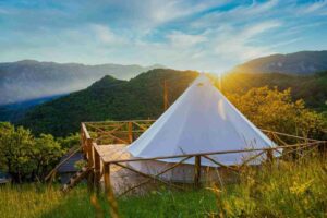 White glamping yurt on a raised platform, surrounded by mountains and forest.